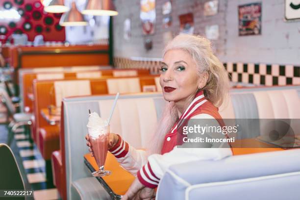 portrait of mature woman in baseball jacket with milkshake in 1950s diner - grey hair cool woman stock-fotos und bilder