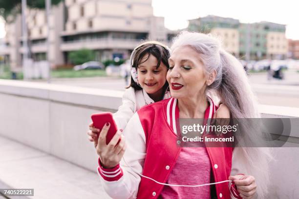 mature woman and girl selecting headphone music in city - young at heart fotografías e imágenes de stock