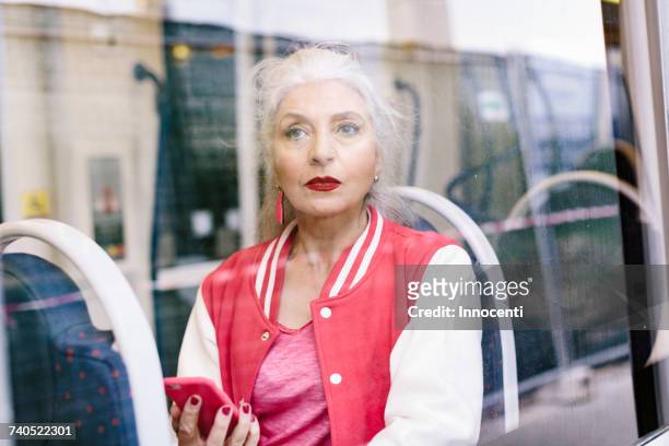 mature woman in baseball jacket looking through window from bus - bus window stock pictures, royalty-free photos & images