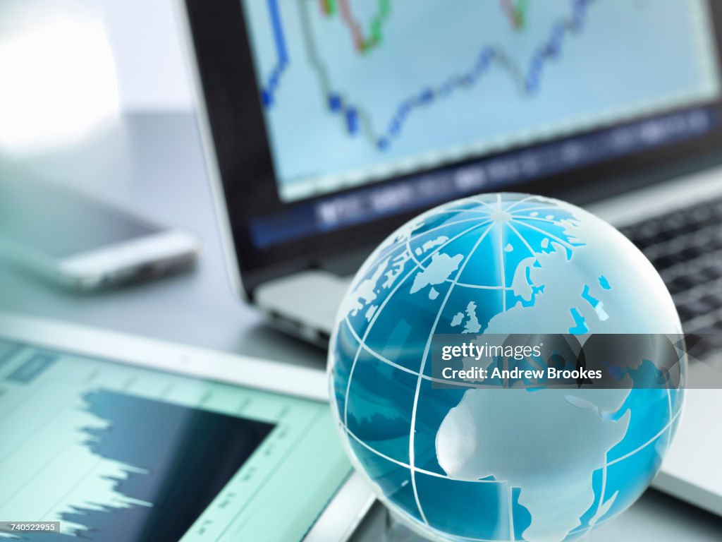 Globe with digital tablet, laptop and smartphone showing international business graphs