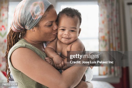 Black mother kissing baby son on cheek Black mother kissing baby son on cheek