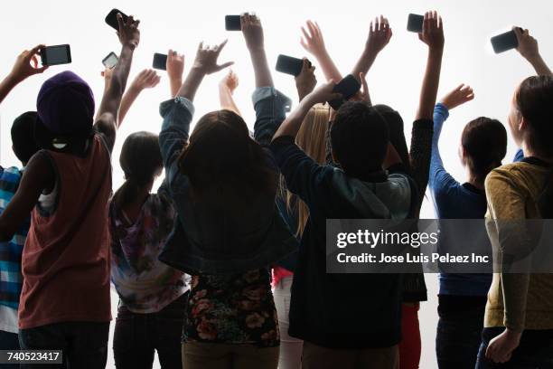 excited boys and girls with arms raised photographing with cell phones - fotografieren stock-fotos und bilder