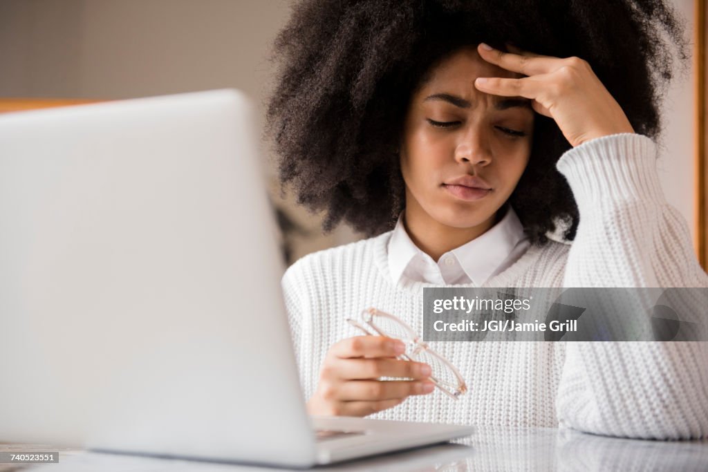 Frustrated African American woman holding eyeglasses near laptop