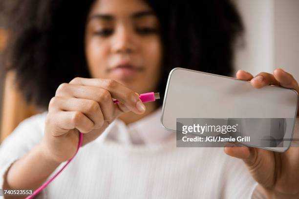 african american woman connecting cable to cell phone - cable stock photos et images de collection