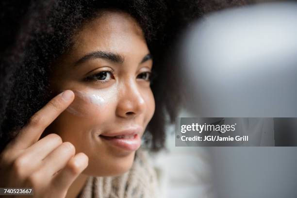 african american woman applying lotion to face - apply stock-fotos und bilder