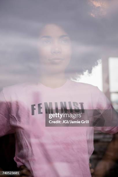 african american woman wearing feminist t-shirt behind window - feminismo fotografías e imágenes de stock