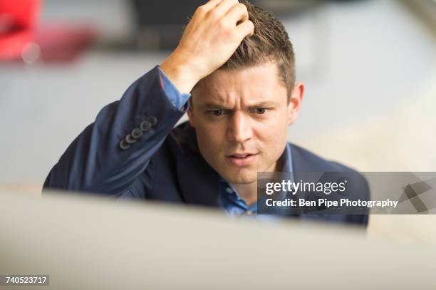 businessman looking at computer in office scratching his head - zich op het hoofd krabben stockfoto's en -beelden