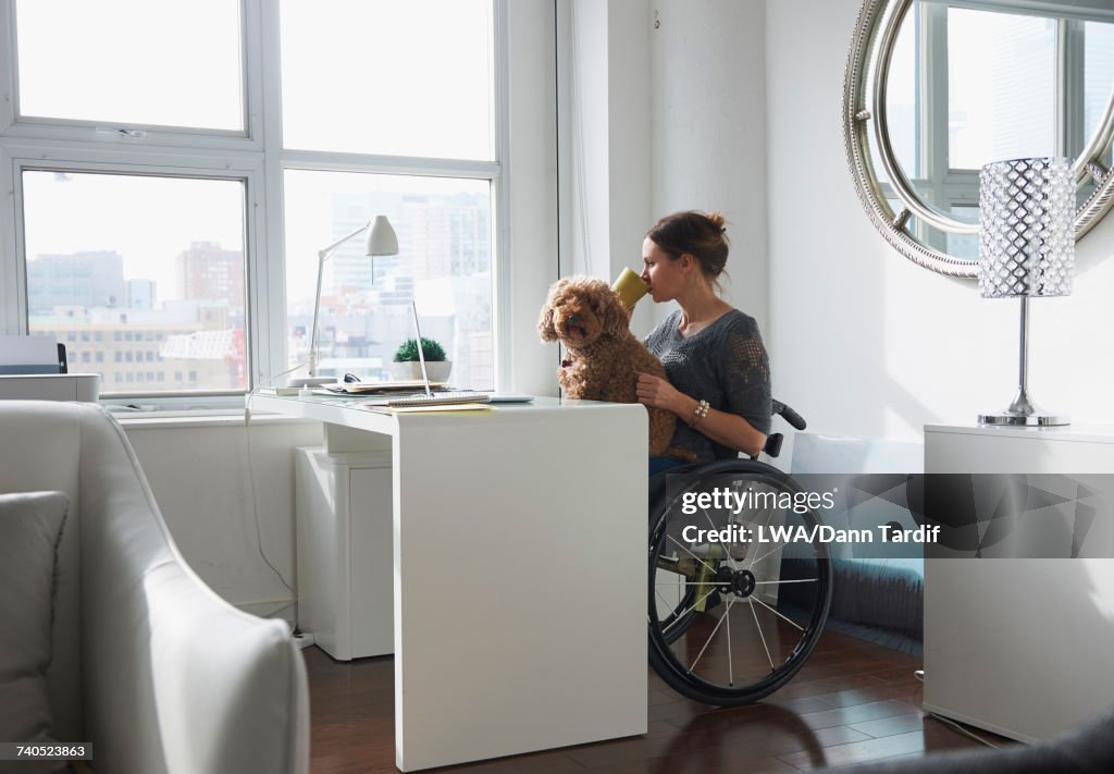 Caucasian woman in wheelchair drinking coffee with dog in lap