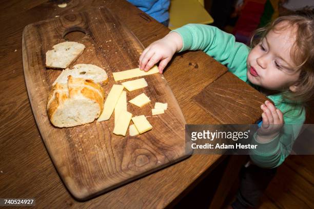 caucasian girl reaching for cheese near bread on cutting board - eating cheese stock-fotos und bilder