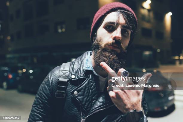portrait of young male hipster on city street at night giving obscene finger gesture - testosterone stockfoto's en -beelden