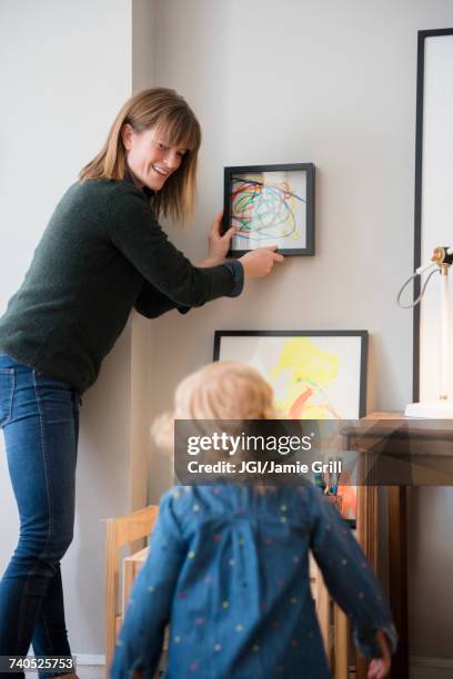 caucasian mother and daughter hanging her painting on wall - hanging art stock pictures, royalty-free photos & images