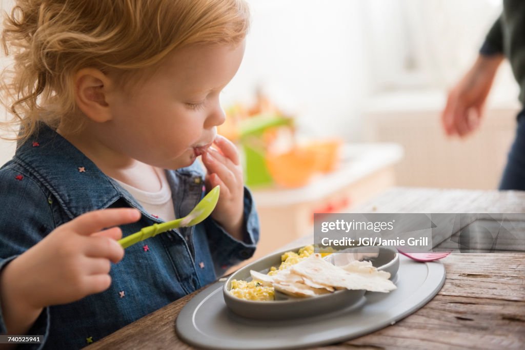 Caucasian girl eating with fingers and spoon