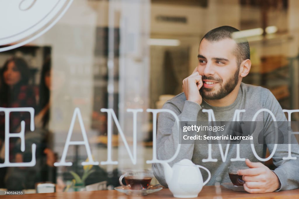 Young man sitting in cafe, view through window