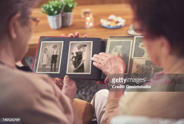 over shoulder view of two senior women looking at old photograph album - looking to the past stock pictures, royalty-free photos & images