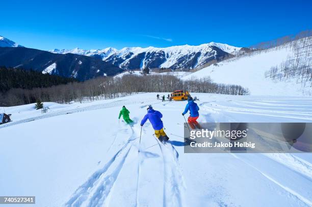 rear view of men skiing down snow covered ski slope, aspen, colorado, usa - aspen stock-fotos und bilder