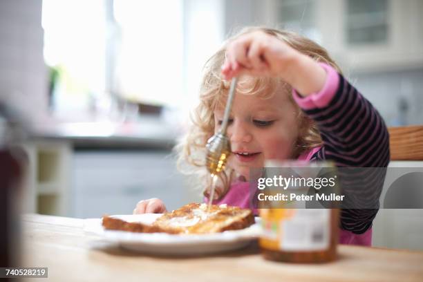 young girl sitting at kitchen table, drizzling honey on toast - honey stock pictures, royalty-free photos & images
