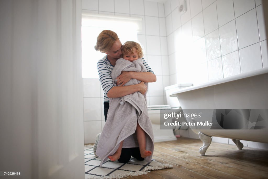 Mother and daughter in bathroom, mother wrapping daughter in bath towel, hugging her