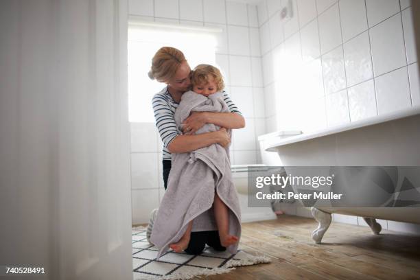 mother and daughter in bathroom, mother wrapping daughter in bath towel, hugging her - asciugare foto e immagini stock