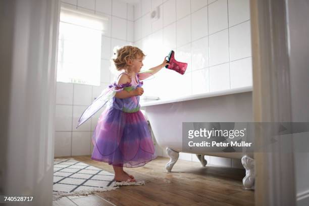 Young girl dressed in fairy costume, holding rubber boot over bathtub