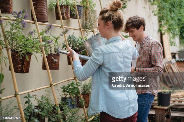Young man and woman tending to plants growing in cans, young woman watering plants using watering can