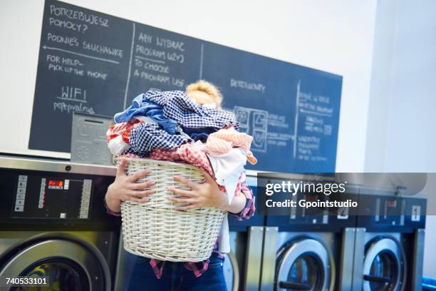 woman in laundrette carrying full laundry basket - laundry basket fotografías e imágenes de stock