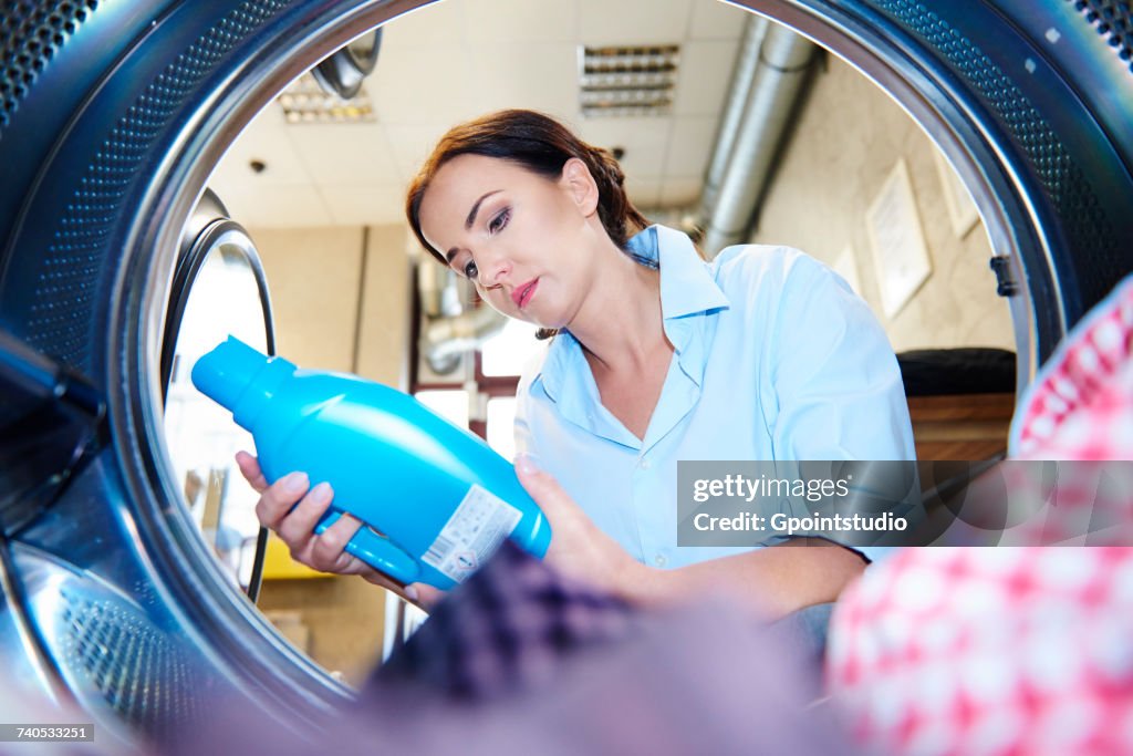 Woman looking at fabric conditioner for washing machine laundry at laundrette