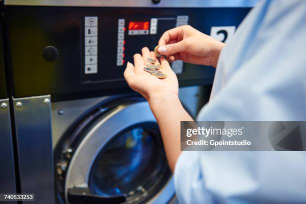 hands of woman selecting coins for washing machine at laundrette - money laundery stockfoto's en -beelden