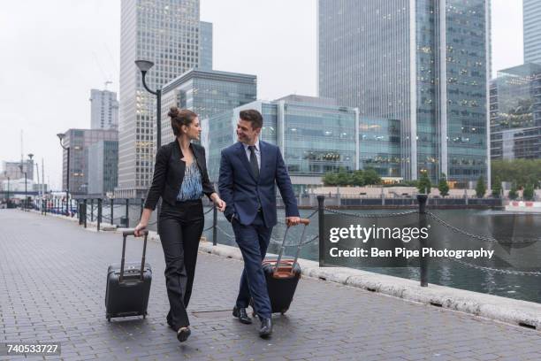 businessman and businesswoman pulling trolley luggage, canary wharf, london, uk - come ストックフォトと画像