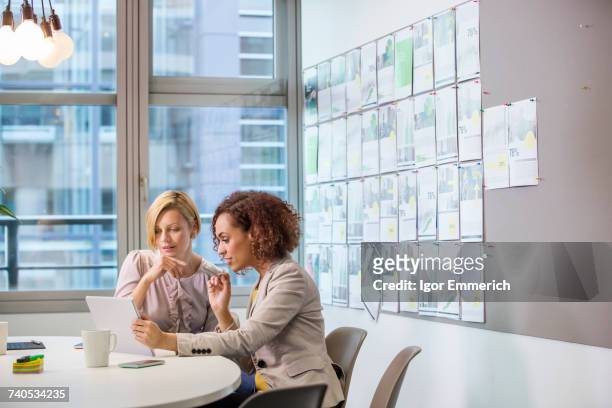 two female digital designers looking at digital tablet at desk - businesswoman in suit jackets stock-fotos und bilder
