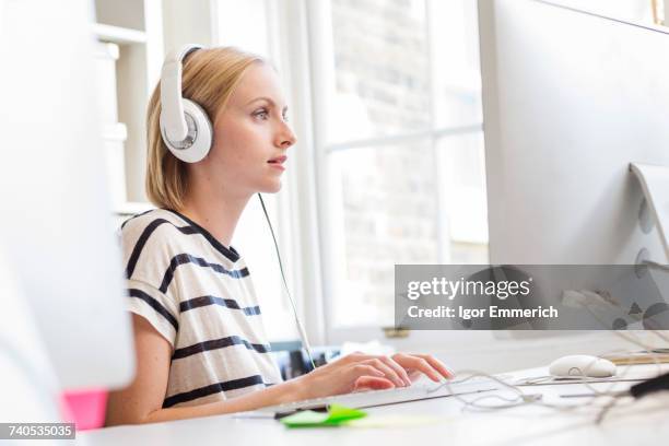 female designer listening to headphones and typing at creative studio desk - inmatningsenhet bildbanksfoton och bilder