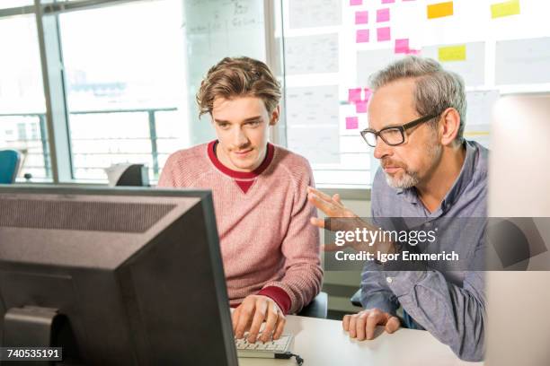 male digital designer explaining design to trainee at office desk - aprendiz fotografías e imágenes de stock