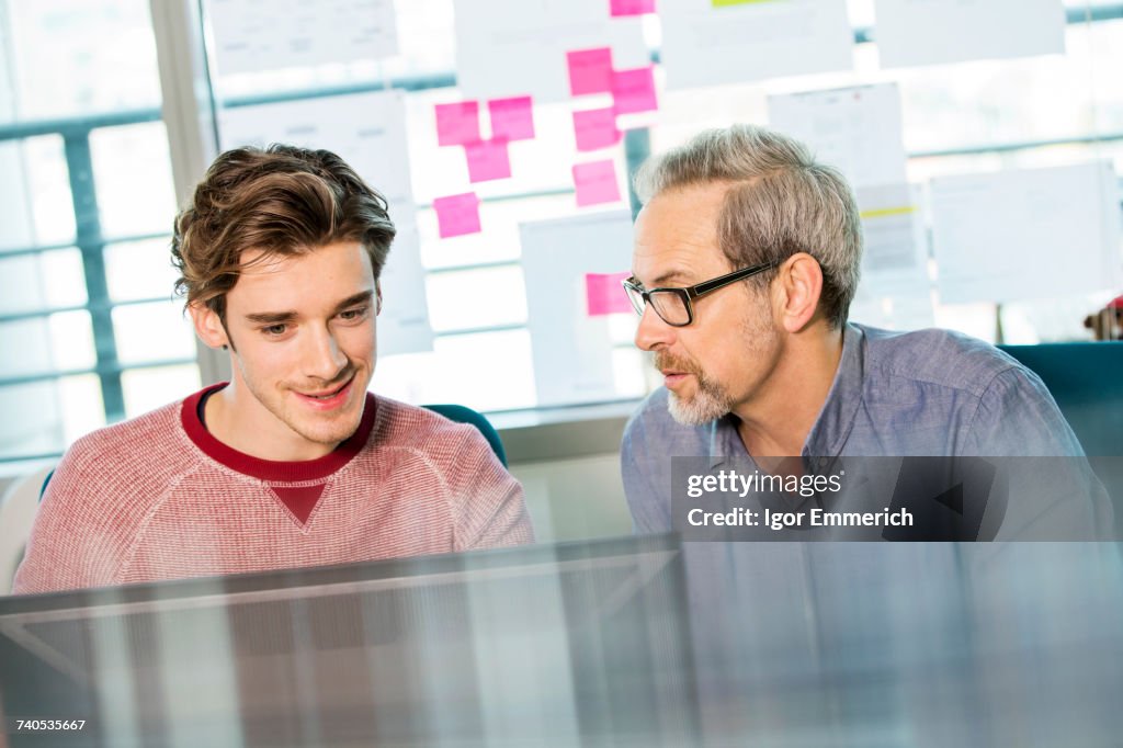 Male digital designer explaining design to trainee at office desk