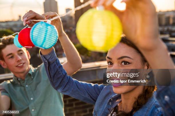 young man and woman hanging lights at roof party in london, uk - party preparation stock pictures, royalty-free photos & images