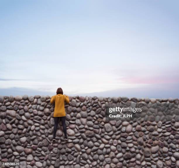 woman holding onto stone wall, looking over top - regarder par dessus photos et images de collection