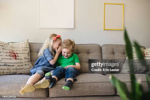 girl on sofa whispering to her brother - child whispering stock-fotos und bilder