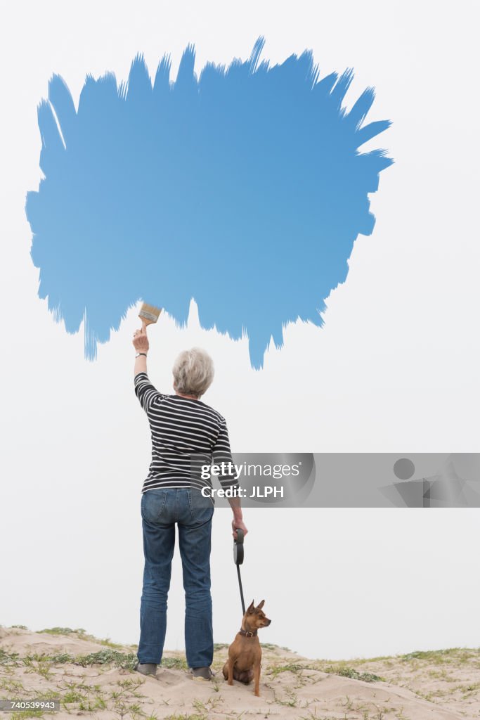 Senior woman with dog on lead painting blue sky in air
