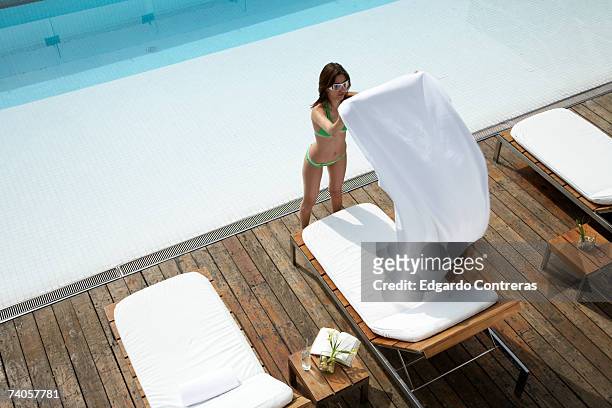 young woman placing towel on sunlounger by swimming pool, high angle view - sun lounger 個照片及圖片檔