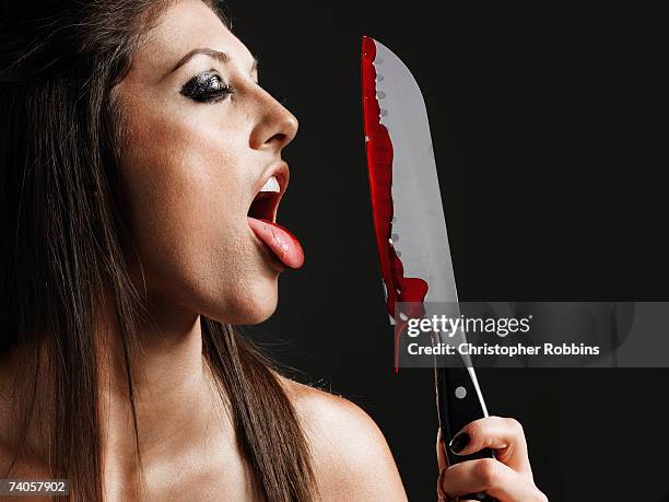 young woman licking blood from knife, close-up, side view - bloody knife stockfoto's en -beelden