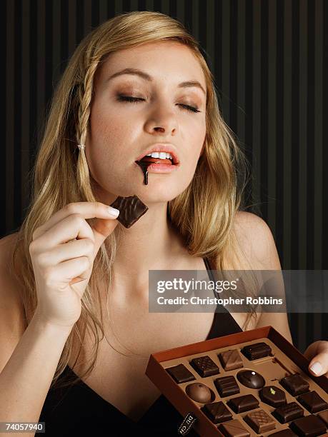 young woman holding box of chocolates, chocolate dripping down chin - box of chocolate foto e immagini stock