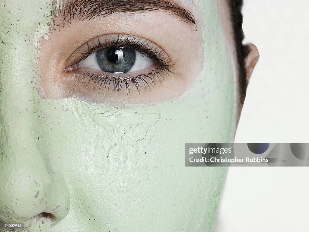 Young woman wearing green facial mask, close-up of eye