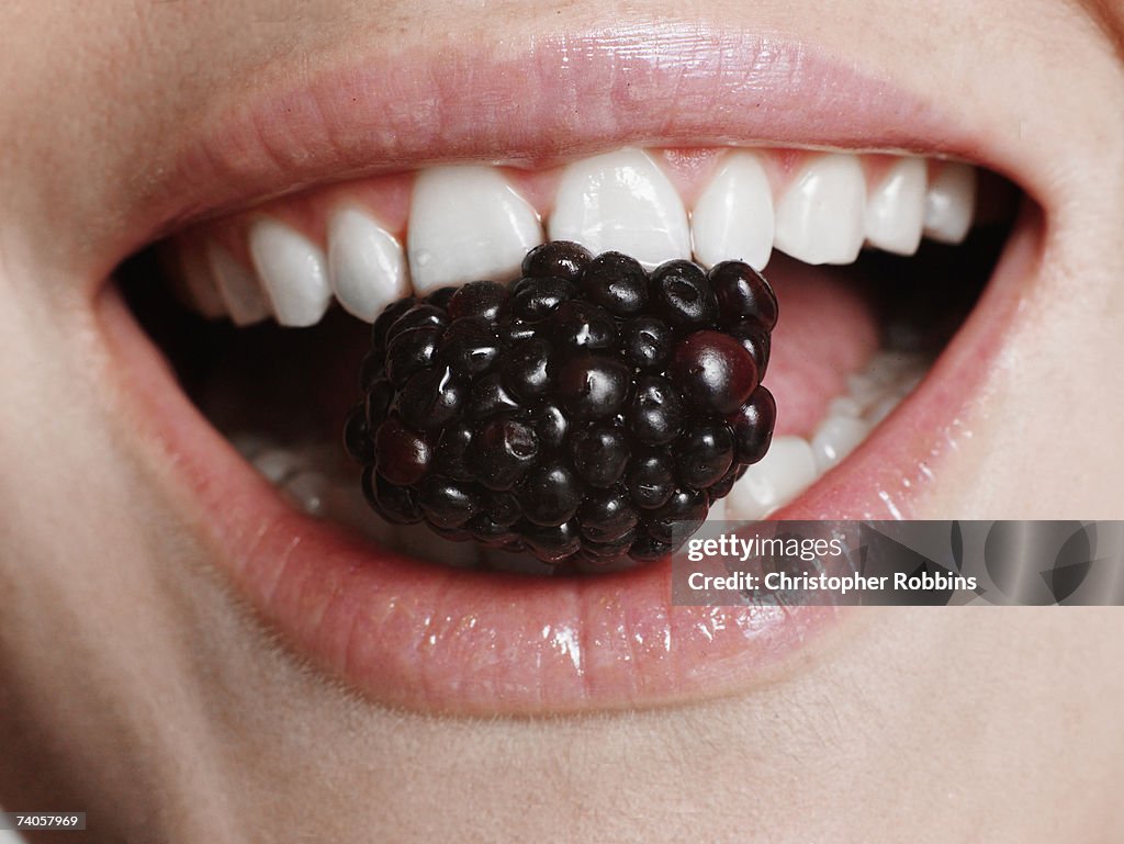 Young woman holding blackberry in teeth, close-up of mouth