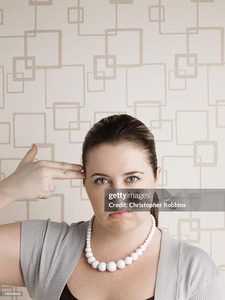 Young plus-size woman miming pistol to head, portrait
