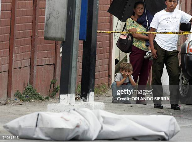 Una pareja y sus hijos permanecen en la escena del crimen donde un conductor y el ayudante de una unidad de transporte urbano fueron asesinados por...