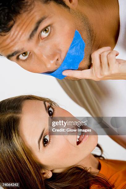 portrait of a mid adult woman with her finger on a young man's lips - man with tape on lips stock pictures, royalty-free photos & images