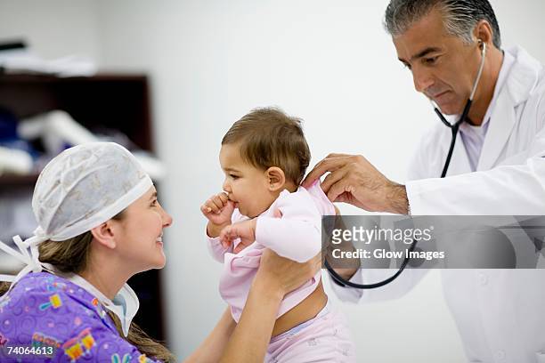 side profile of a female doctor playing with a baby girl and a male doctor examining her - surgical mask profile stock pictures, royalty-free photos & images