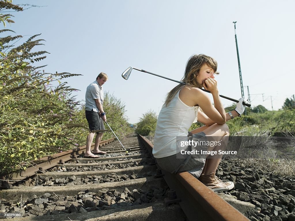 Man on woman playing golf on railway track