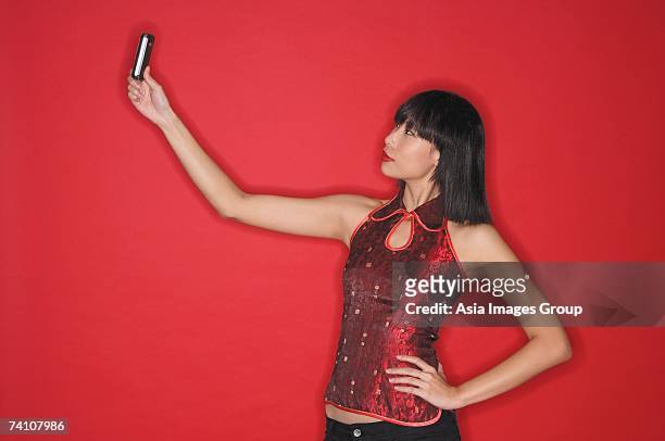 woman using mobile phone to take a picture of herself, hand on hip - chinese people posing for camera stockfoto's en -beelden