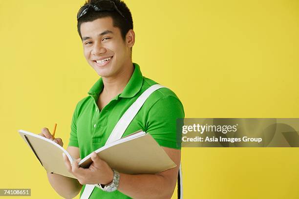 young man writing in notebook, looking at camera - sling bag stock pictures, royalty-free photos & images