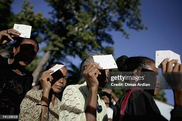 East Timorese people cover their face from the sun with their voting cards or IDs as the queue at a polling station as East Timorese people vote in a...
