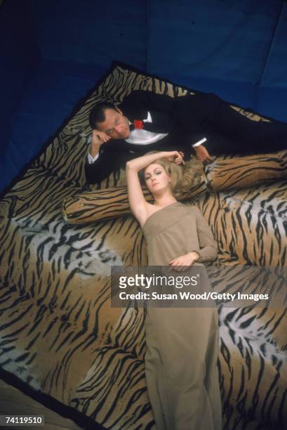 Portrait of American fashion designer Bill Blass , dressed in a tuxedo with a carnation in his lapel, as he reclines on a tiger print rug with an...